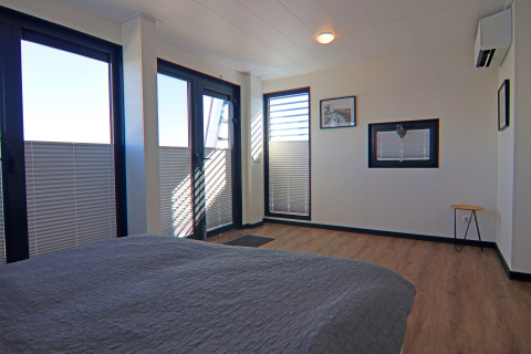 Modern houseboat bedroom with large windows, wood flooring, minimal furniture and natural light.