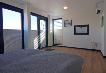 Moderne soveværelse på en husbåd med store vinduer, trægulv og minimalistisk indretning.