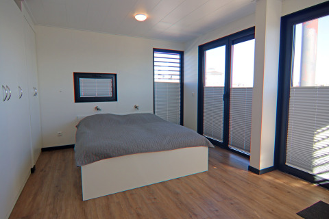Bedroom on a houseboat with double bed, wood floor, large windows and modern, bright decor.