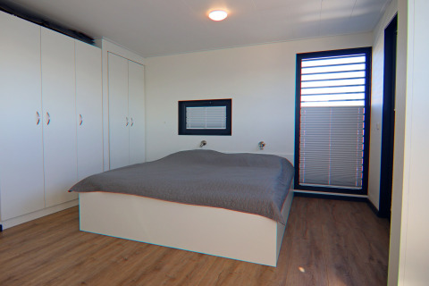 Houseboat bedroom with wooden floor, large wardrobes, double bed and big window with blinds.