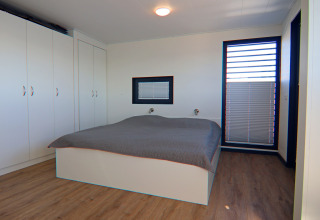 Houseboat bedroom with wooden floor, large wardrobes, double bed and big window with blinds.