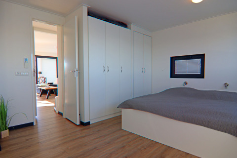 Bright modern bedroom on a houseboat with large wardrobes, a double bed, and a view into the living area.