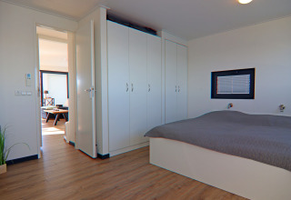 Bright modern bedroom on a houseboat with large wardrobes, a double bed, and a view into the living area.