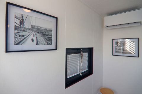Room on a houseboat with two framed photos, a small window, and an air conditioner on the white wall.