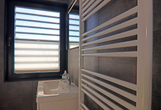 Bathroom on a houseboat with window, small sink, soap dispenser and a white towel radiator in the foreground.