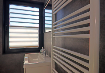 Baño en una casa flotante con ventana, lavabo pequeño, dispensador de jabón y radiador toallero blanco.