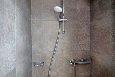 Modern shower area on a houseboat featuring decorative grey tiles and an adjustable showerhead.