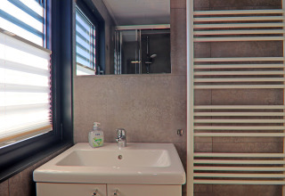 Modern bathroom on a houseboat with a sink, mirror, heated towel rail, window blind, and hand soap.