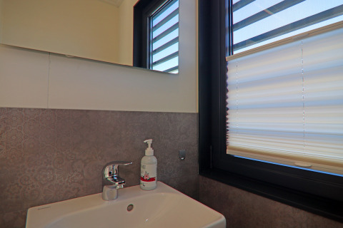 Modern bathroom sink with soap dispenser beside a window with blinds on a houseboat bathroom.
