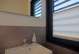 Modern bathroom sink with soap dispenser beside a window with blinds on a houseboat bathroom.