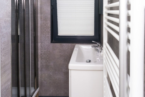 Modern narrow bathroom on a houseboat with a sink, window with blinds, and shower cabin beside it.