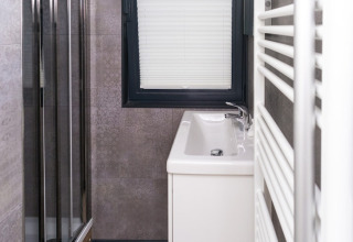 Modern narrow bathroom on a houseboat with a sink, window with blinds, and shower cabin beside it.
