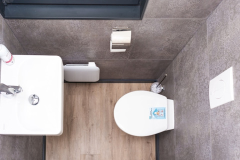 Top view of a houseboat bathroom showing a toilet, sink, toilet paper holder, and wood flooring.