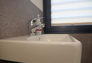 Modern sink with chrome faucet and soap dispenser next to a window on a houseboat in Germany.