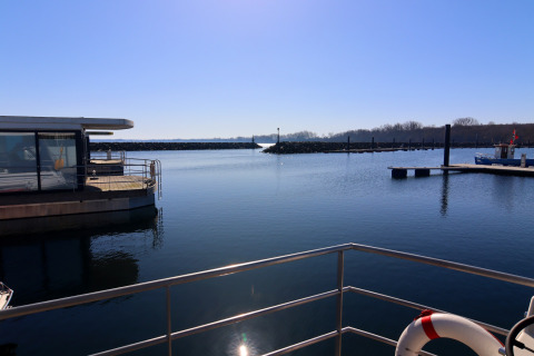 View from a houseboat overlooking a calm harbor under clear blue skies and tranquil water.