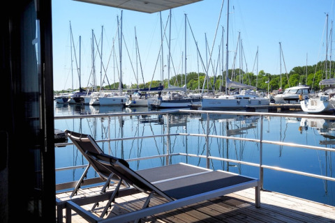 View from a houseboat deck with two lounge chairs, overlooking a marina full of moored sailboats.