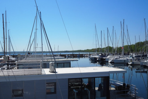 View from a houseboat in a marina with several sailboats docked under a clear blue sky on a sunny day.