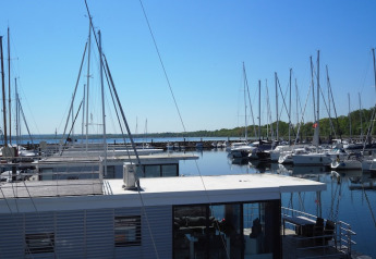 Vista desde una casa flotante en un puerto deportivo con varios veleros y cielo azul en un día soleado.