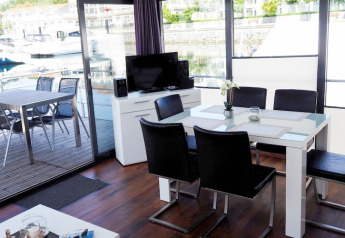 Zona de comedor y salón moderna en una casa flotante con vistas a la terraza y al puerto deportivo, amueblada elegante.