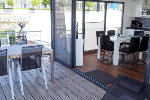 View from a houseboat with a wooden deck, outdoor dining table, and a modern indoor dining area and kitchen.