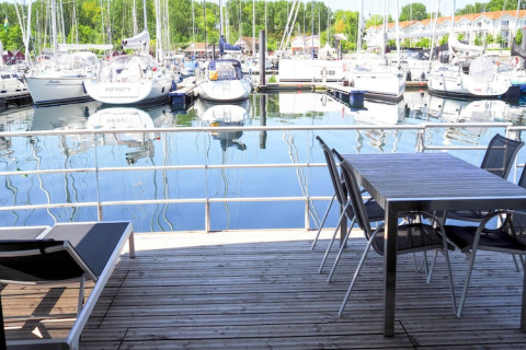 View from a houseboat deck with table, chairs, and lounger overlooking a marina filled with sailboats.