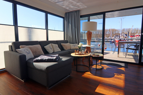 Modern houseboat living room with sectional sofa, view of water and boats through large glass doors.