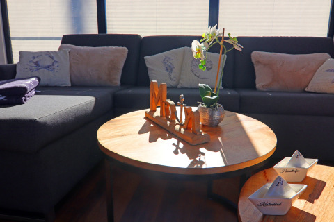 Houseboat living room with gray sectional sofa, cozy cushions, flower, and sunlight on wooden table.