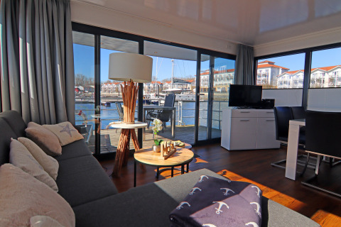 Living room of houseboat 'Family & Friends LP 1' in Germany with marina view through glass doors.