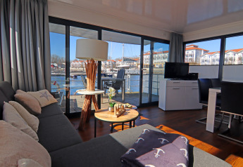 Salón de la casa flotante 'Family & Friends LP 1' en Alemania con vistas al puerto desde puertas de cristal.