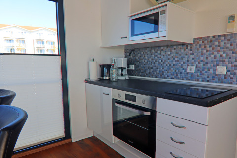 Modern kitchenette on houseboat with oven, stovetop, microwave, mosaic backsplash, and natural light.