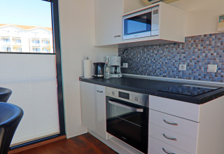 Modern kitchenette on houseboat with oven, stovetop, microwave, mosaic backsplash, and natural light.
