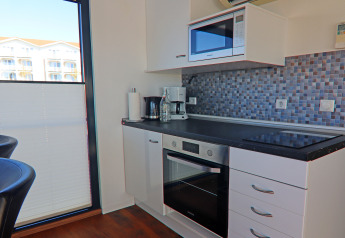 Moderne kitchenette op woonboot met oven, kookplaat, microgolf en mozaïektegels met daglicht.