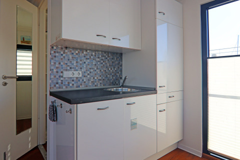 Modern kitchenette on a houseboat with glossy white cabinets, mosaic tile backsplash, and large window.