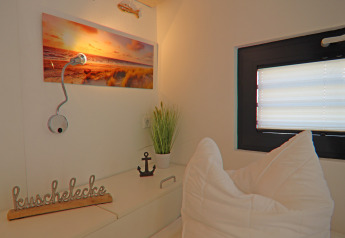 Rincón acogedor en una casa flotante con cojines, decoración, ventana, arte y lámpara de lectura.