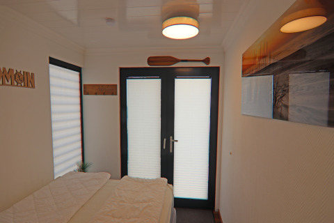 Houseboat bedroom with double doors, nautical wall decor, window, and cozy overhead ceiling light.