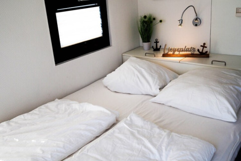 Cozy double bed on a houseboat, featuring white bedding, pillows, a lamp, and a small plant decor.