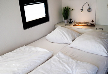 Cama doble acogedora en un barco casa con ropa de cama blanca, cojines, ventana y decoración náutica.