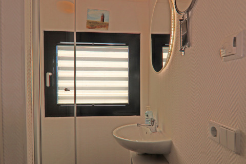 Houseboat bathroom with a sink, round mirror, striped window blind, light wall pattern, and small painting.