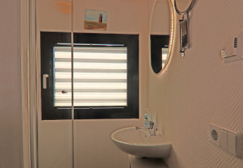 Cuarto de baño en una casa flotante con lavabo, espejo redondo, persiana y cuadro en la pared clara.