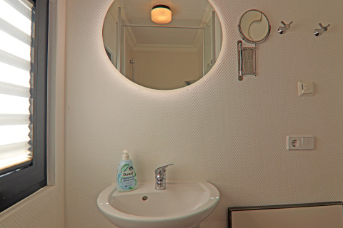Modern houseboat bathroom with round mirror, sink, soap dispenser, coat hooks, and natural light.