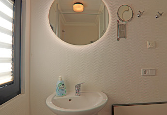 Bagno moderno in una houseboat con specchio rotondo, lavandino, dispenser di sapone e luce naturale.