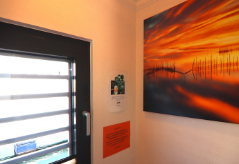 Esquina interior de una casa flotante con ventana moderna, pintura de atardecer y notas en la pared.