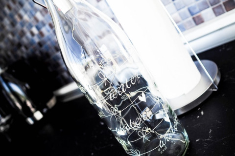 Glass bottle with the word 'water' written on it, standing on a dark kitchen counter in a houseboat.