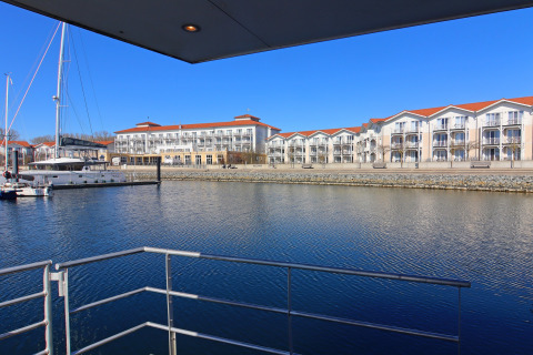 View from a houseboat overlooking a marina with sailboats and modern apartments on a sunny day.