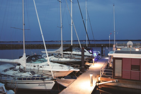 Evening photo of yachts and a houseboat docked at a pier in Germany under a peaceful blue sky.