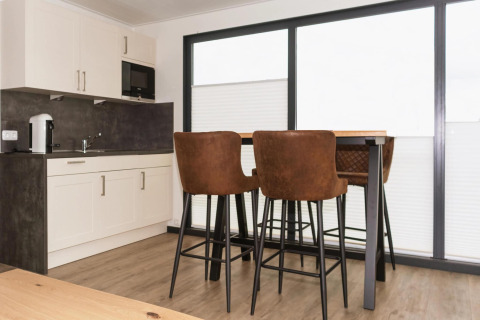 Modern houseboat kitchen with white cabinets, dark countertop, and a dining table with brown barstools in Germany.