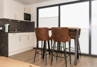 Modern houseboat kitchen with white cabinets, dark countertop, and a dining table with brown barstools in Germany.