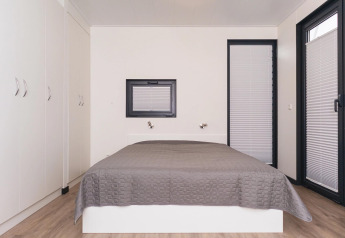 Dormitorio moderno en la casa flotante 'Family & Friends mit Hund LP 10', decoración neutra y colcha gris.