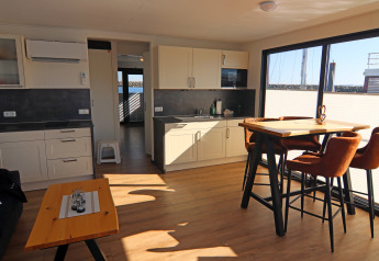 Intérieur de péniche moderne avec cuisine, salle à manger, grandes fenêtres et plancher en bois clair.