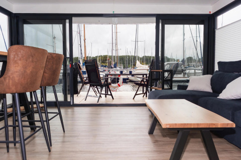 Moderne husbåd stue med udsigt til marinaen, udendørs siddeplads og både i baggrunden i Tyskland.